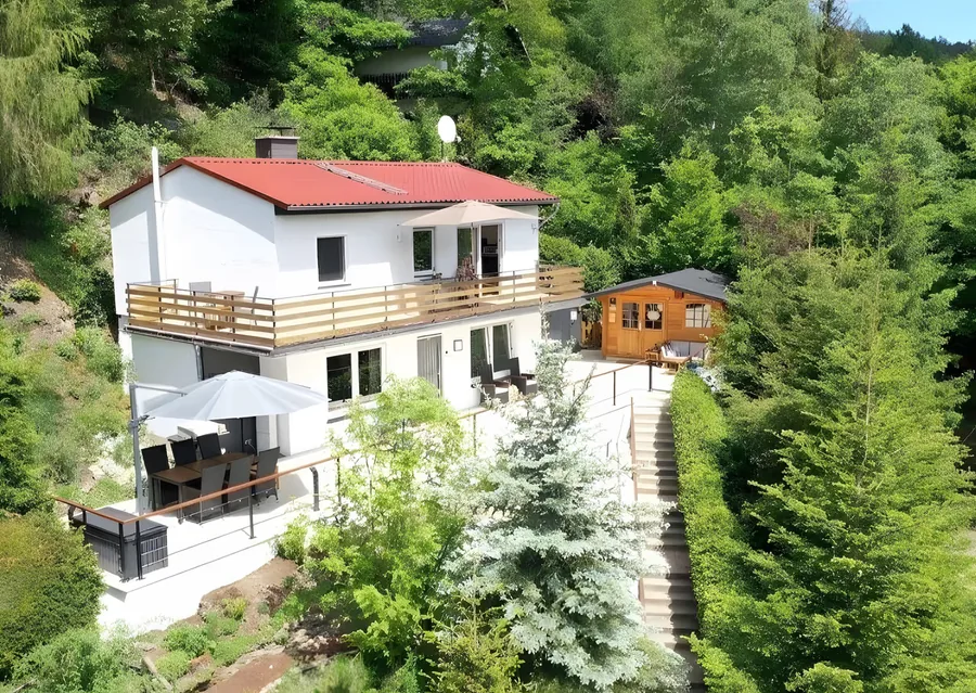 Luftbild des Ferienhauses mit Balkon im Obergeschoss, Terrasse darunter und Gartenhaus im Garten